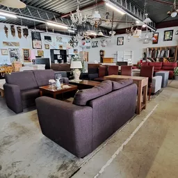 Winkelvloer met uitgestalde zitmeubels, tafels en kroonluchters in kringloopwinkel