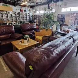 Inrichting van een kringloopwinkel met bruinleren zitmeubels, houten tafel en boekenkasten op de achtergrond