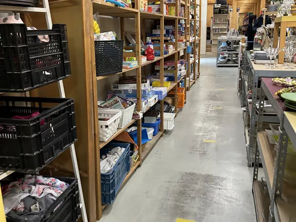 Winkelinterieur met houten stellingen vol dozen, kratjes en spullen, grijze betonvloer, geel afzetlint op de grond