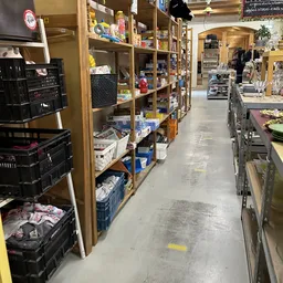 Winkelinterieur met houten stellingen vol dozen, kratjes en spullen, grijze betonvloer, geel afzetlint op de grond