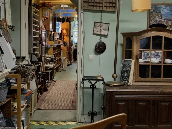 Smalle winkelgang met houten kasten, vintage items en spullen aan de wanden in een kringloopwinkel