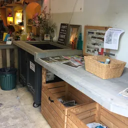 Werkplek in kringloopwinkel met toonbank, opbergmanden, kranten en diverse spullen op en onder het werkblad