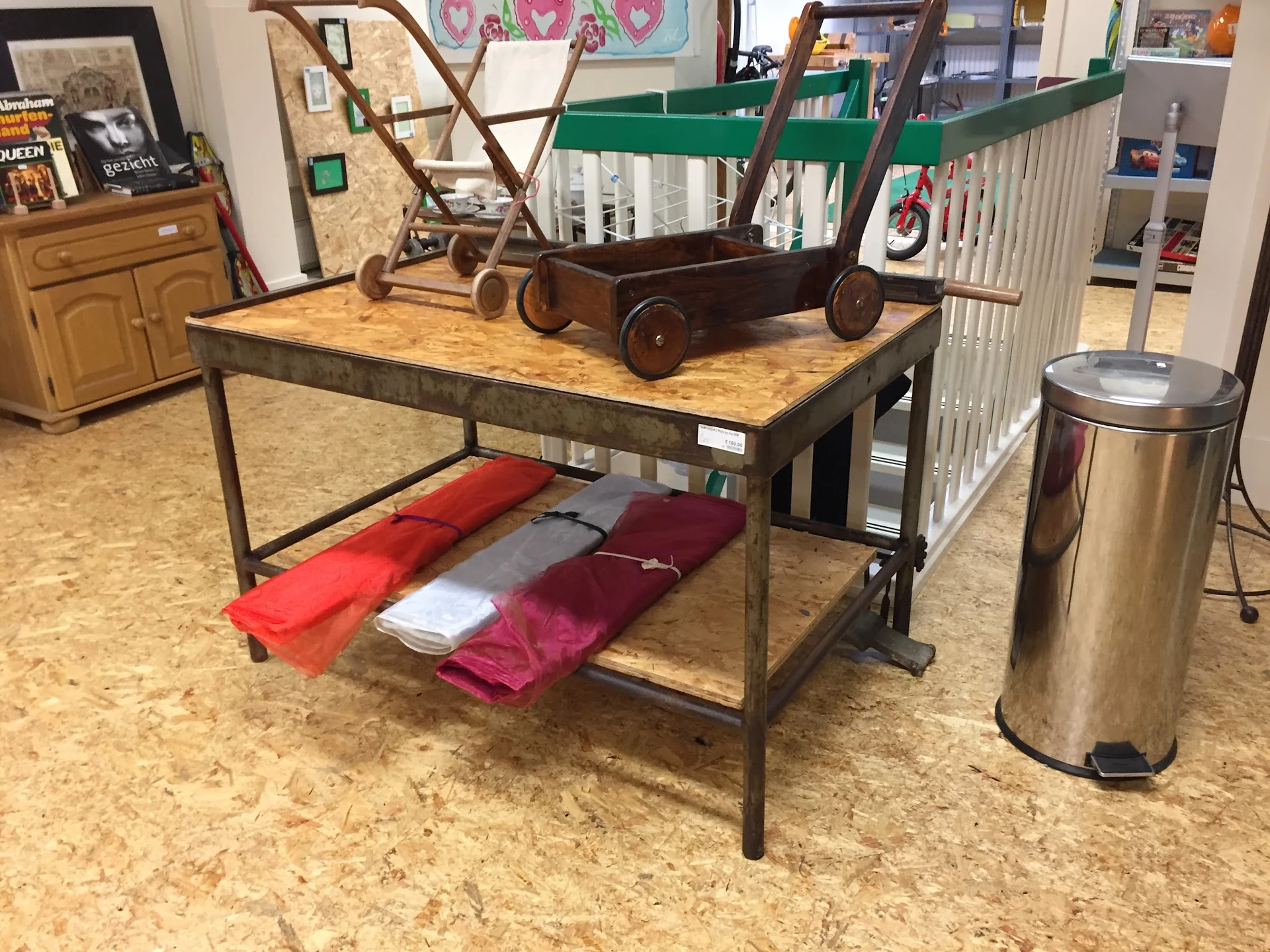 Industriële tafel met houten blad en verschillende tweedehands huishoudartikelen en meubels op de winkelvloer