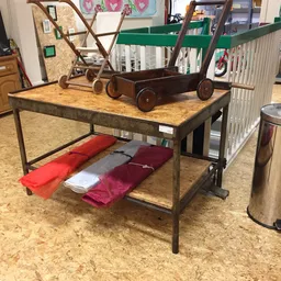 Industriële tafel met houten blad en verschillende tweedehands huishoudartikelen en meubels op de winkelvloer