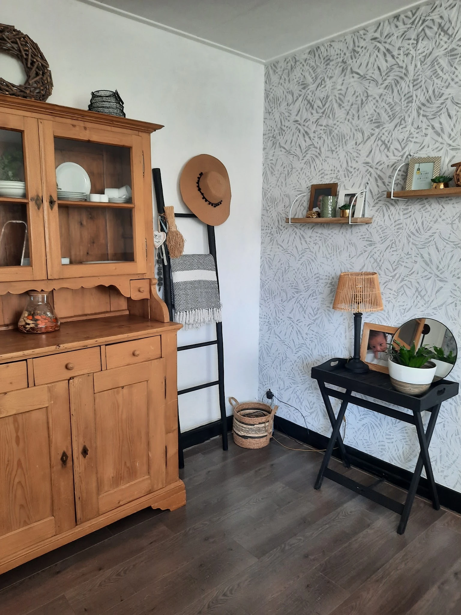 Ingerichte winkelhoek met houten vintage kast, zwart tafeltje, wanddecoratie en planken met woonaccessoires