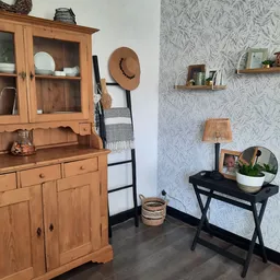 Ingerichte winkelhoek met houten vintage kast, zwart tafeltje, wanddecoratie en planken met woonaccessoires