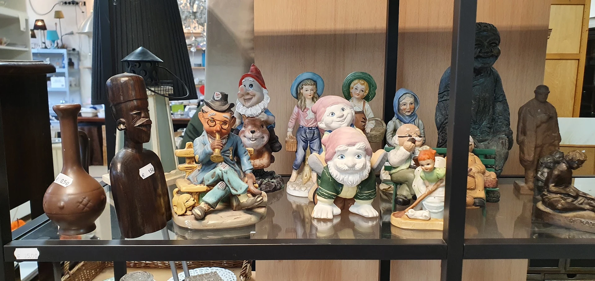 Verzameling vintage beeldjes en figuurjes in een glazen vitrinekast, waaronder kabouters, boeren en andere decoratieve items