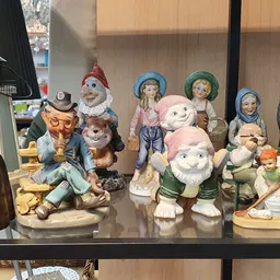 Verzameling vintage beeldjes en figuurjes in een glazen vitrinekast, waaronder kabouters, boeren en andere decoratieve items