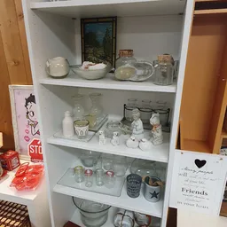 Witte boekenplank met diverse huishoudelijke spullen: vazen, glazen potten, beeldjes en decoratiestukken.
