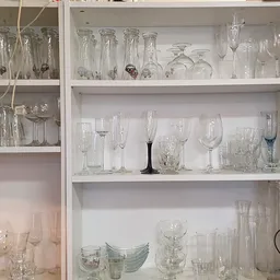 Glazenkast met diverse glazen en drinkglazen uitgestald op witte planken
