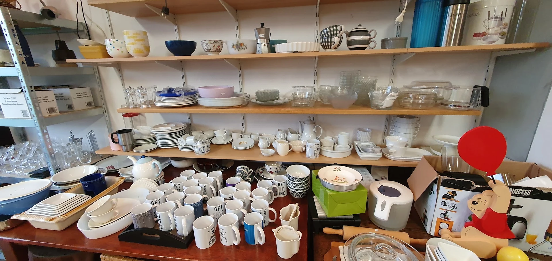 Schappen en toonbank vol met serviesgoed, kopjes, kannen en huishoudartikelen