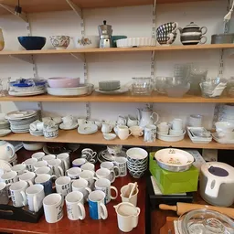 Schappen en toonbank vol met serviesgoed, kopjes, kannen en huishoudartikelen