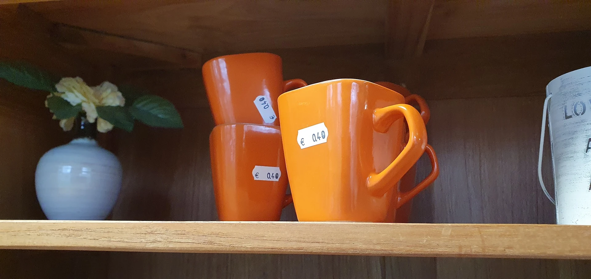 Drie oranje keramische kannen of kruiken met prijsstickers op een houten plank