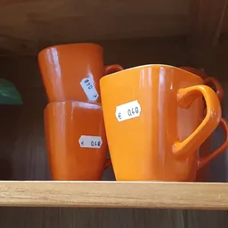 Drie oranje keramische kannen of kruiken met prijsstickers op een houten plank