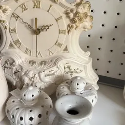 Witte decoratieve items met gaten en een witte barokke klok met gouden details in een kringloopwinkel