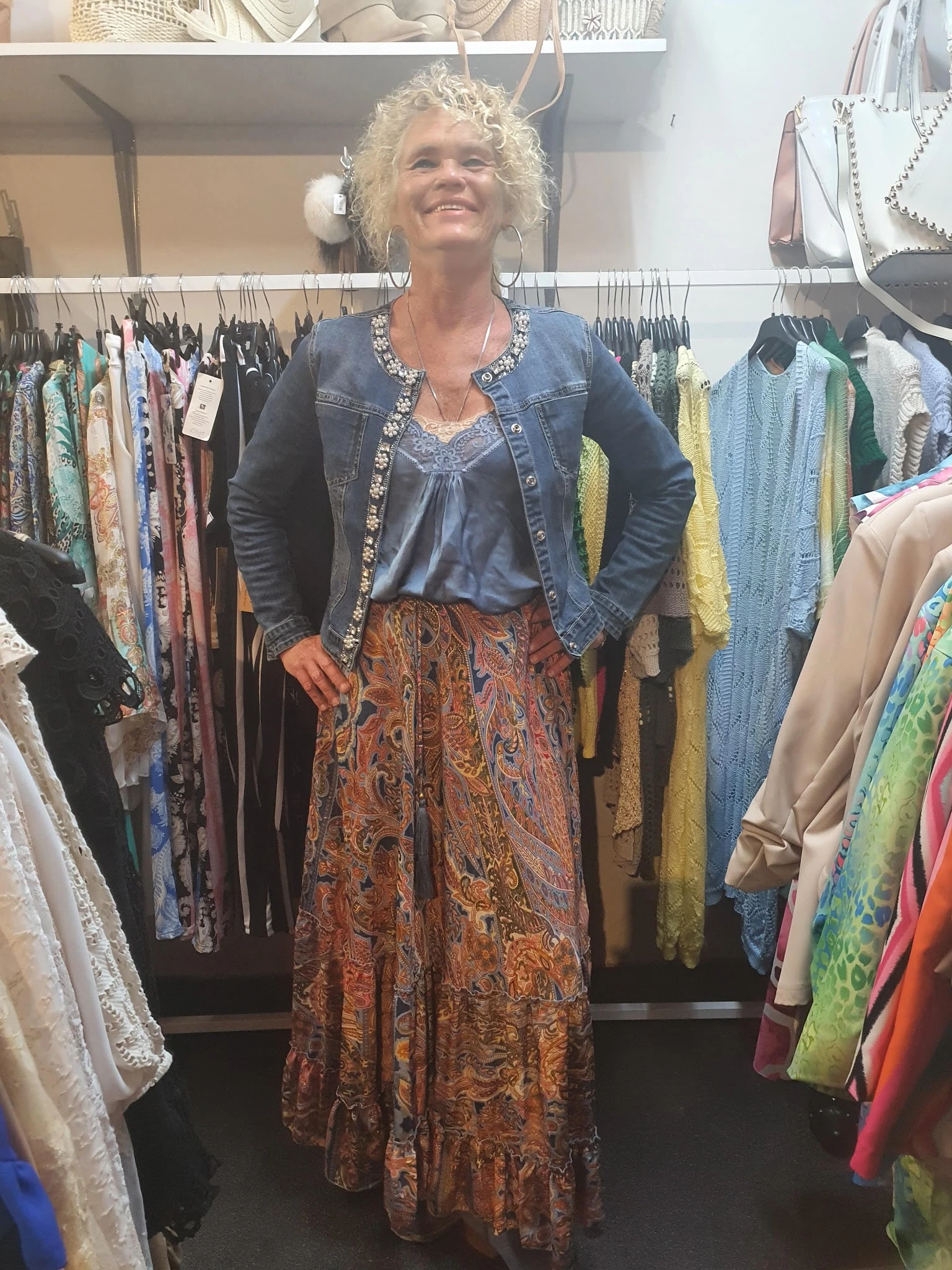 Vrouw toont outfit bestaande uit denim jasje, blauw top en patroon rok in kringloopwinkel