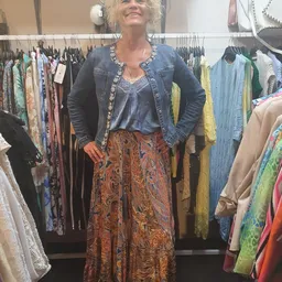 Vrouw toont outfit bestaande uit denim jasje, blauw top en patroon rok in kringloopwinkel