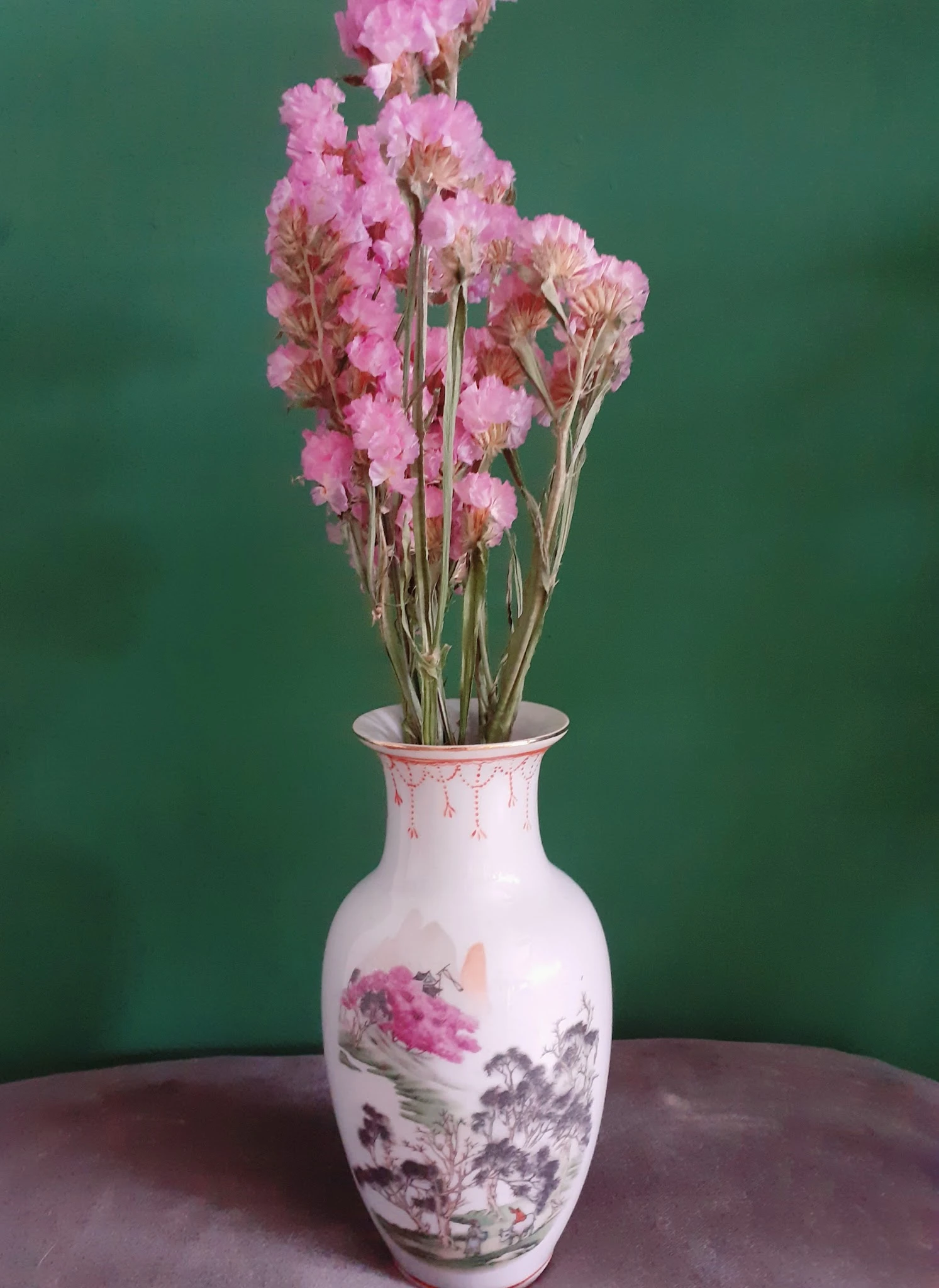 Witte vaas met roze bloemenprint en gedroogde roze bloemen tegen groene achtergrond