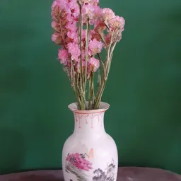 Witte vaas met roze bloemenprint en gedroogde roze bloemen tegen groene achtergrond