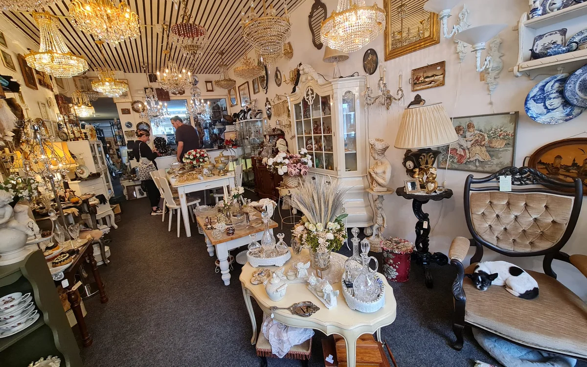 Winkelinterieur met vintage meubels, decoratieve objecten, goudkleurige hangende lampen en diverse spullen op tafels
