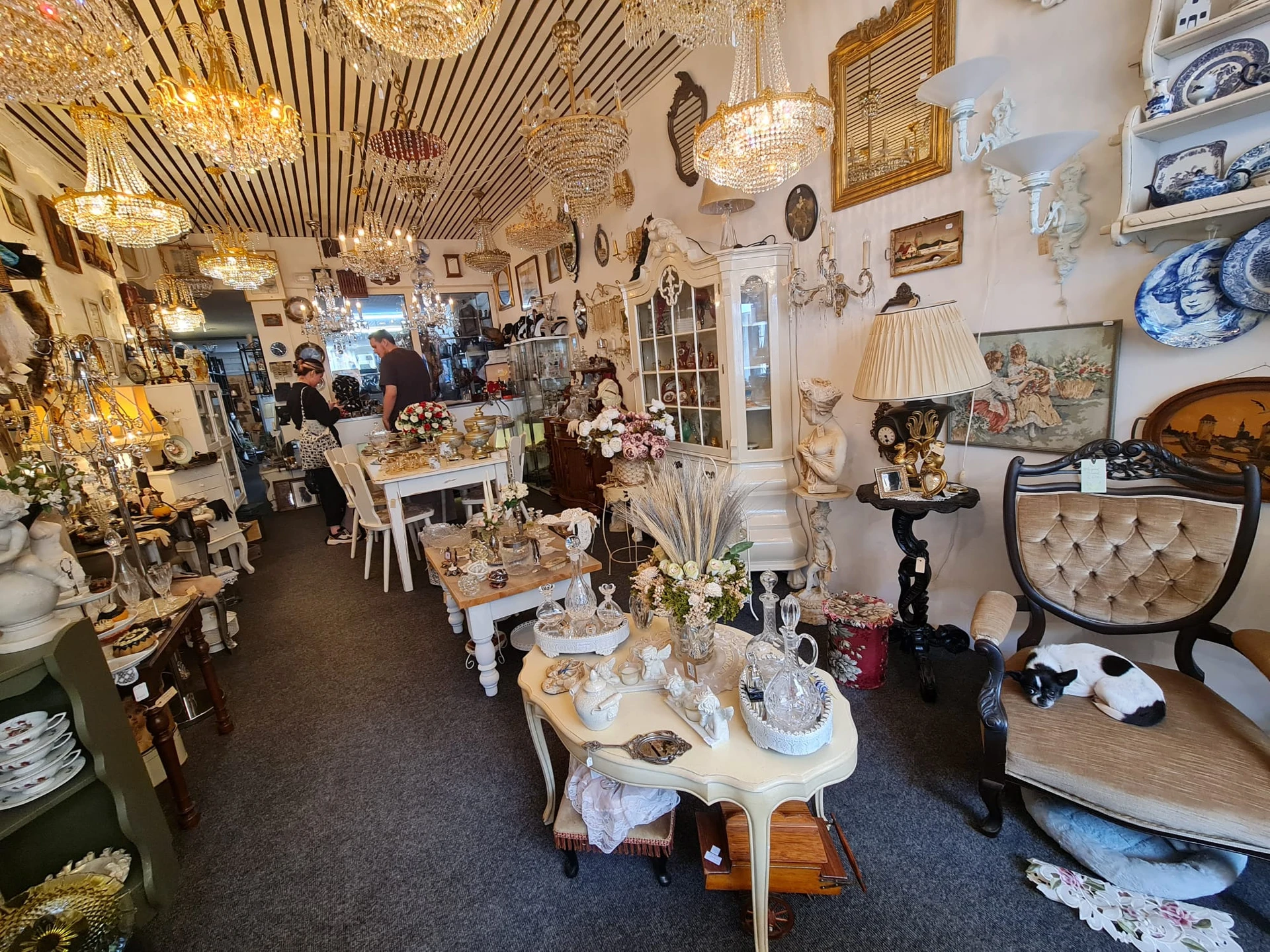 Winkelinterieur met vintage meubels, decoratieve objecten, goudkleurige hangende lampen en diverse spullen op tafels