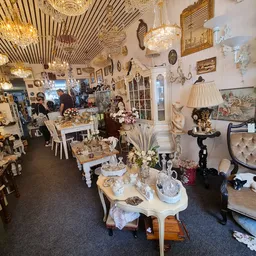 Winkelinterieur met vintage meubels, decoratieve objecten, goudkleurige hangende lampen en diverse spullen op tafels