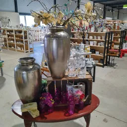 Twee zilveren urnen met bloemstukken en glazen op een houten tafel in de kringloopwinkel