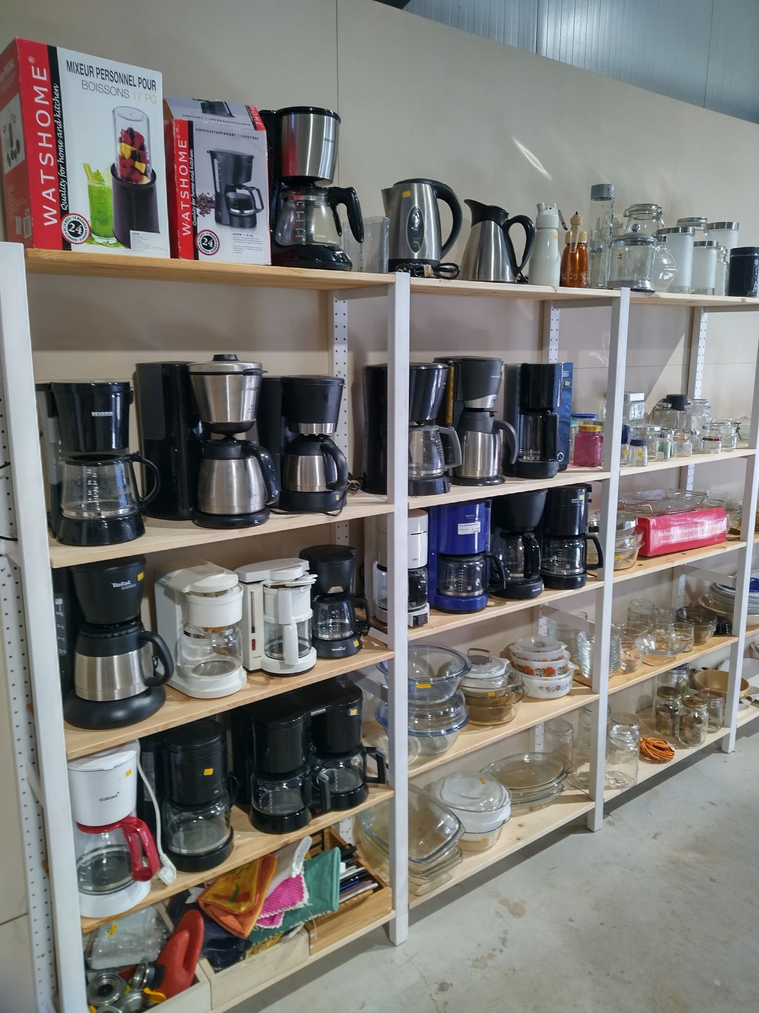 Stellingen met verschillende koffiezetapparaten en huishoudelijke apparaten in een kringloopwinkel