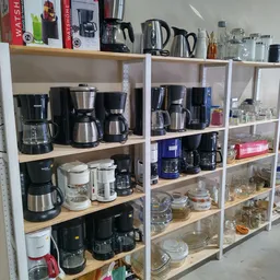 Stellingen met verschillende koffiezetapparaten en huishoudelijke apparaten in een kringloopwinkel