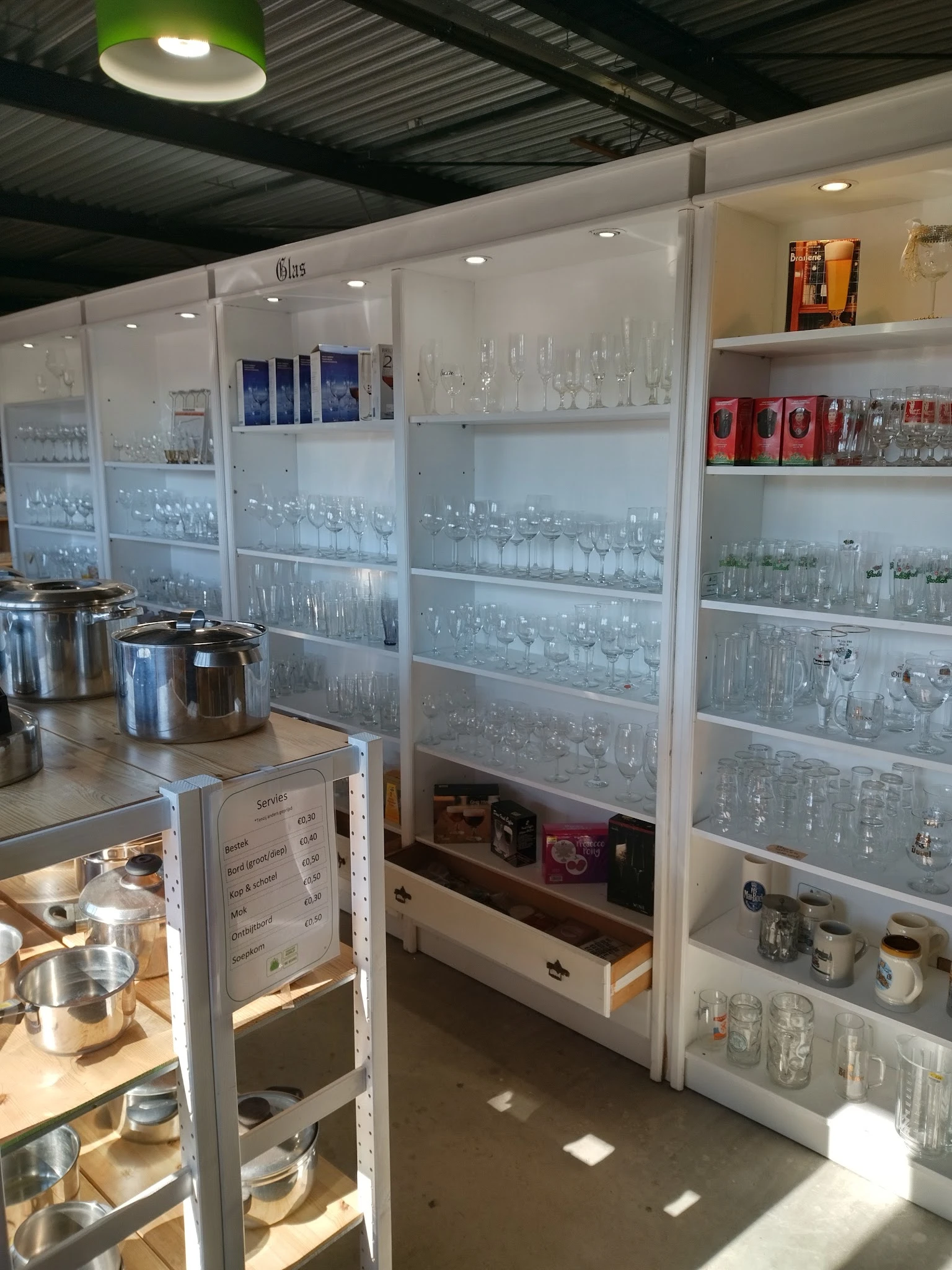 Glazen vitrinekasten met diverse glaswerk en serviesgoed in een kringloopwinkel