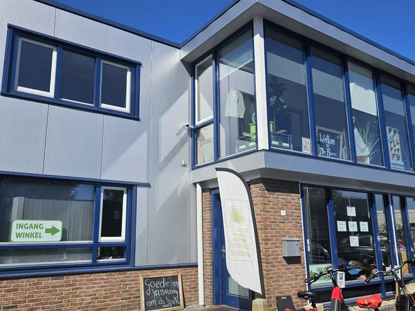 Moderne gevel van kringloopwinkel met blauwe ramen en deuren, baksteenwerk onderaan, zonnig weer