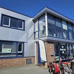 Moderne gevel van kringloopwinkel met blauwe ramen en deuren, baksteenwerk onderaan, zonnig weer
