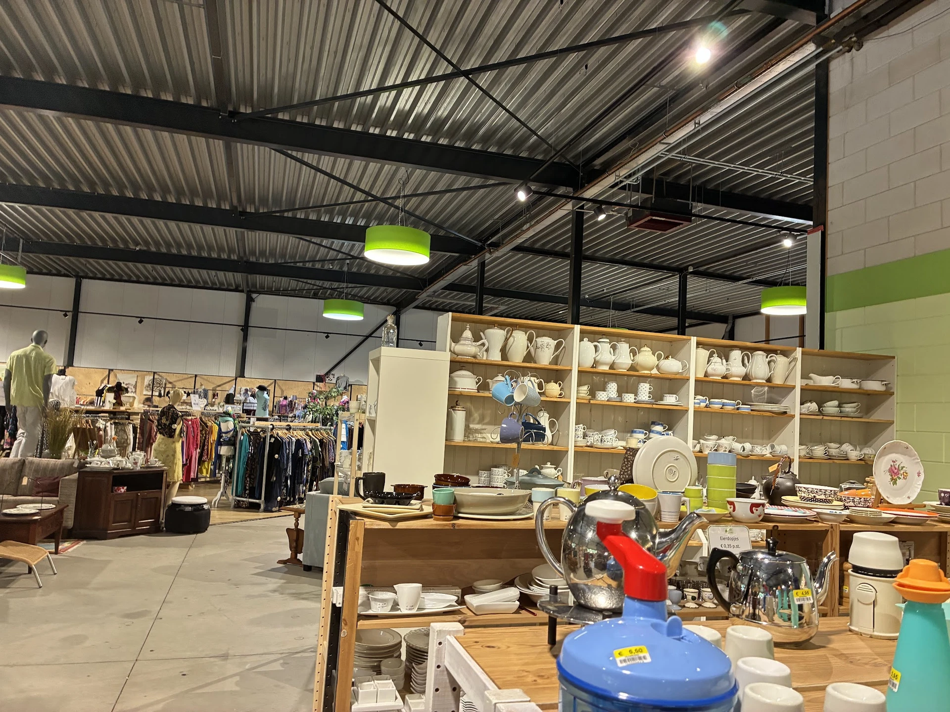 Winkelvloer met huishoudelijke artikelen, servies op stellingen en kledingrekken in een kringloopwinkel
