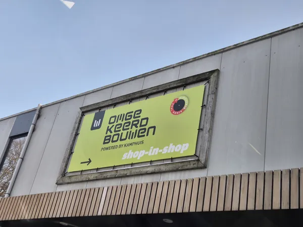 Gevel van kringloopwinkel met geel bord en shop-shop-logo