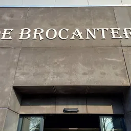 Grijze betonnen gevel met witte letters 'DE BROCANTERIE' en donkere ingang eronder