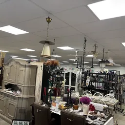 Ruim interieur van kringloopwinkel met stellingen vol spullen, hangende lampen, meubels en diverse artikelen