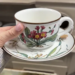 Vintage porseleinen kopje en schotel met bloemendessin, gehouden in een hand