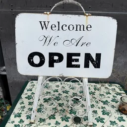Wit bord met zwarte tekst 'Welcome We Are OPEN' op een groene basis