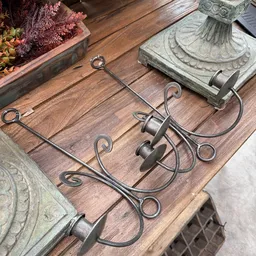 Drie smeedijzeren kandelaars met sierlijke krullen op houten tafel