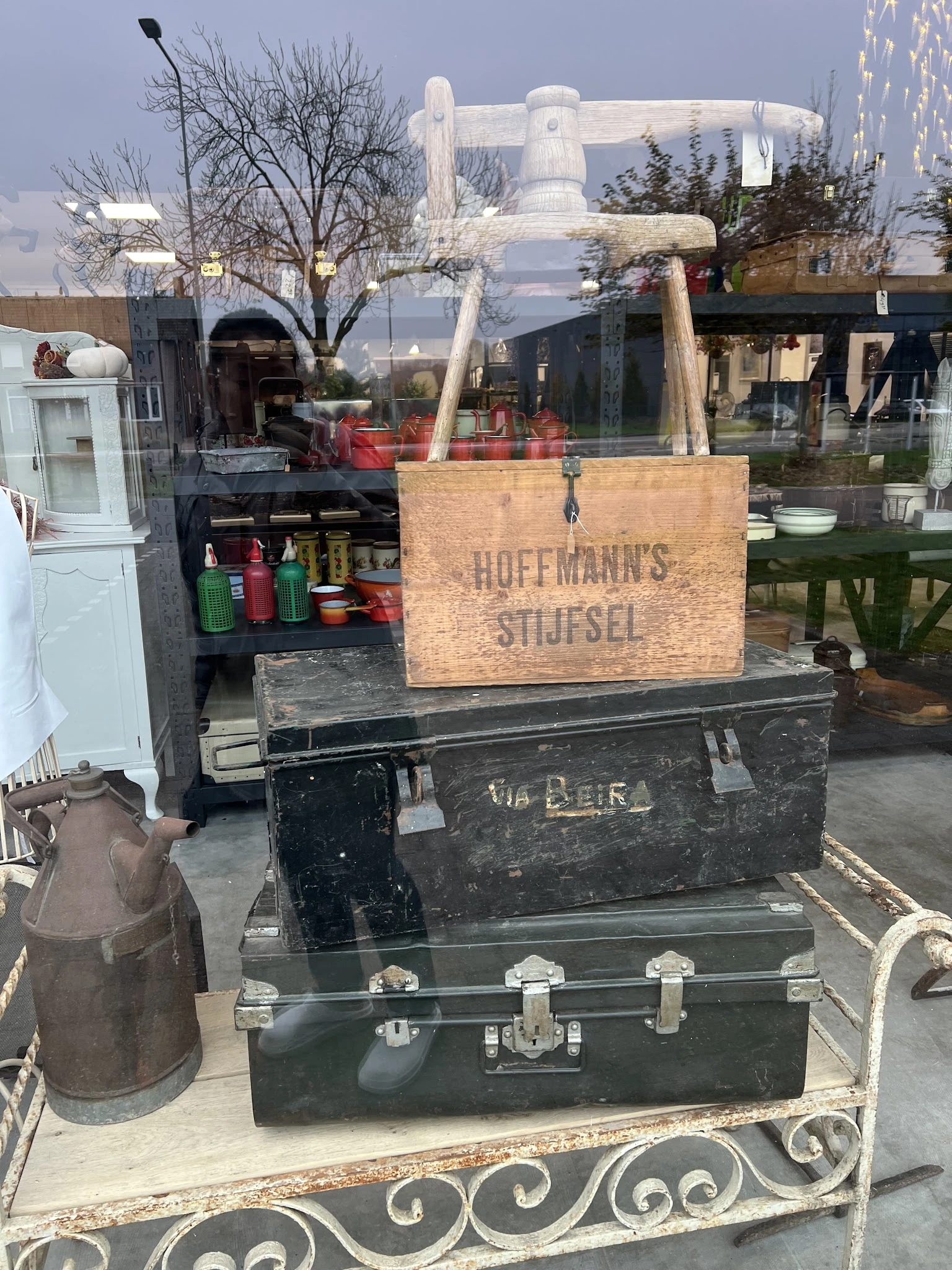 Uitgestalde vintage kisten en antieke dozen op een terras, waaronder een houten Hoffmanns Stijfsel kist