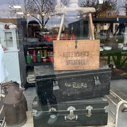 Uitgestalde vintage kisten en antieke dozen op een terras, waaronder een houten Hoffmanns Stijfsel kist