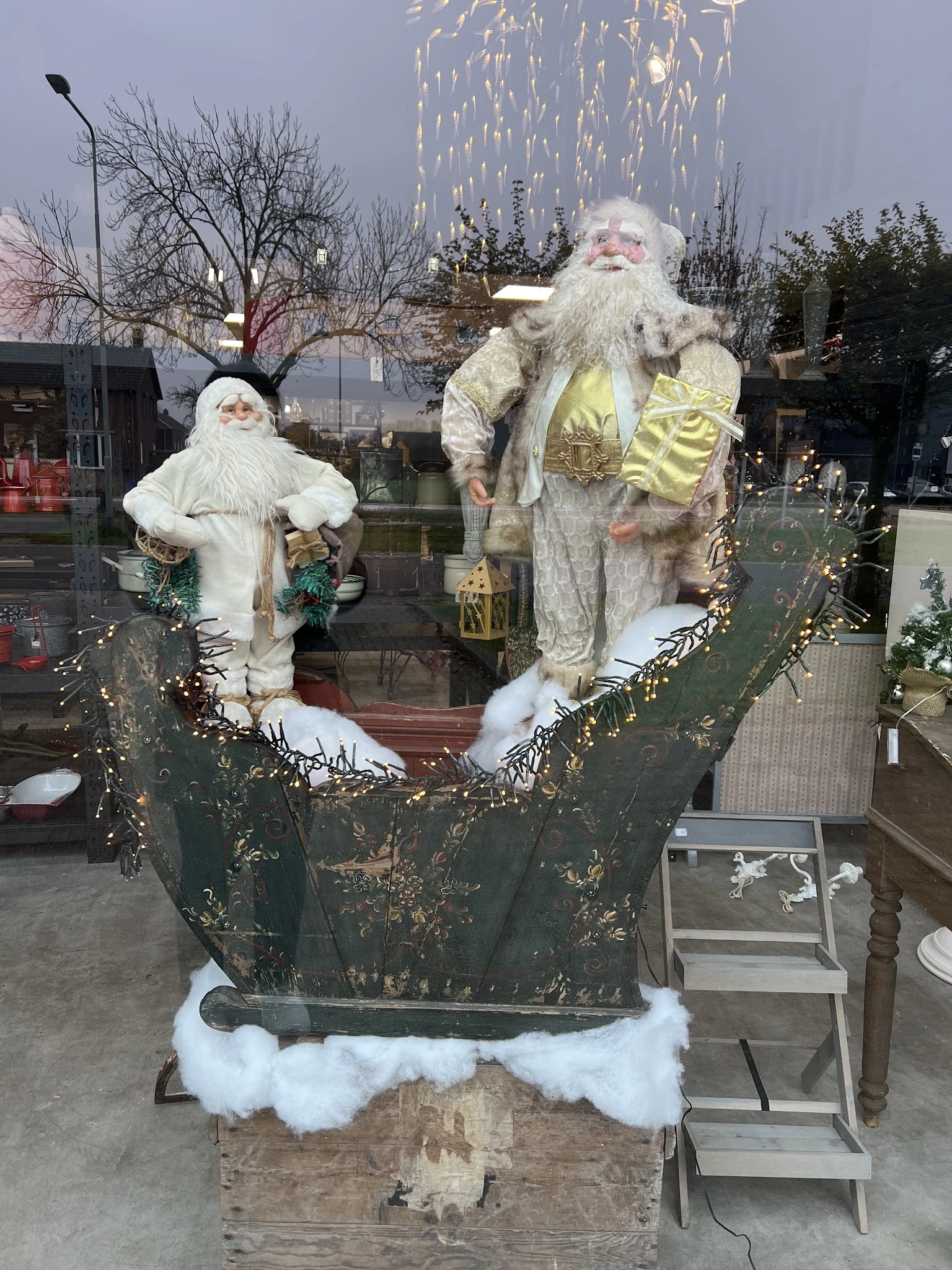 Kerstdecoratie met twee kerstmanfiguren in wit en goud, opgezet in een groen decoratief arrangement met gouden slingers