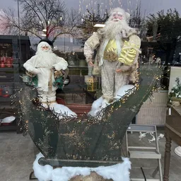 Kerstdecoratie met twee kerstmanfiguren in wit en goud, opgezet in een groen decoratief arrangement met gouden slingers