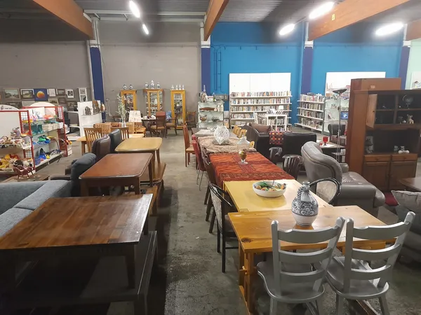 Winkelvloer met diverse meubels: houten eettafels, stoelen, kasten en boekenkasten tegen blauwe wanden
