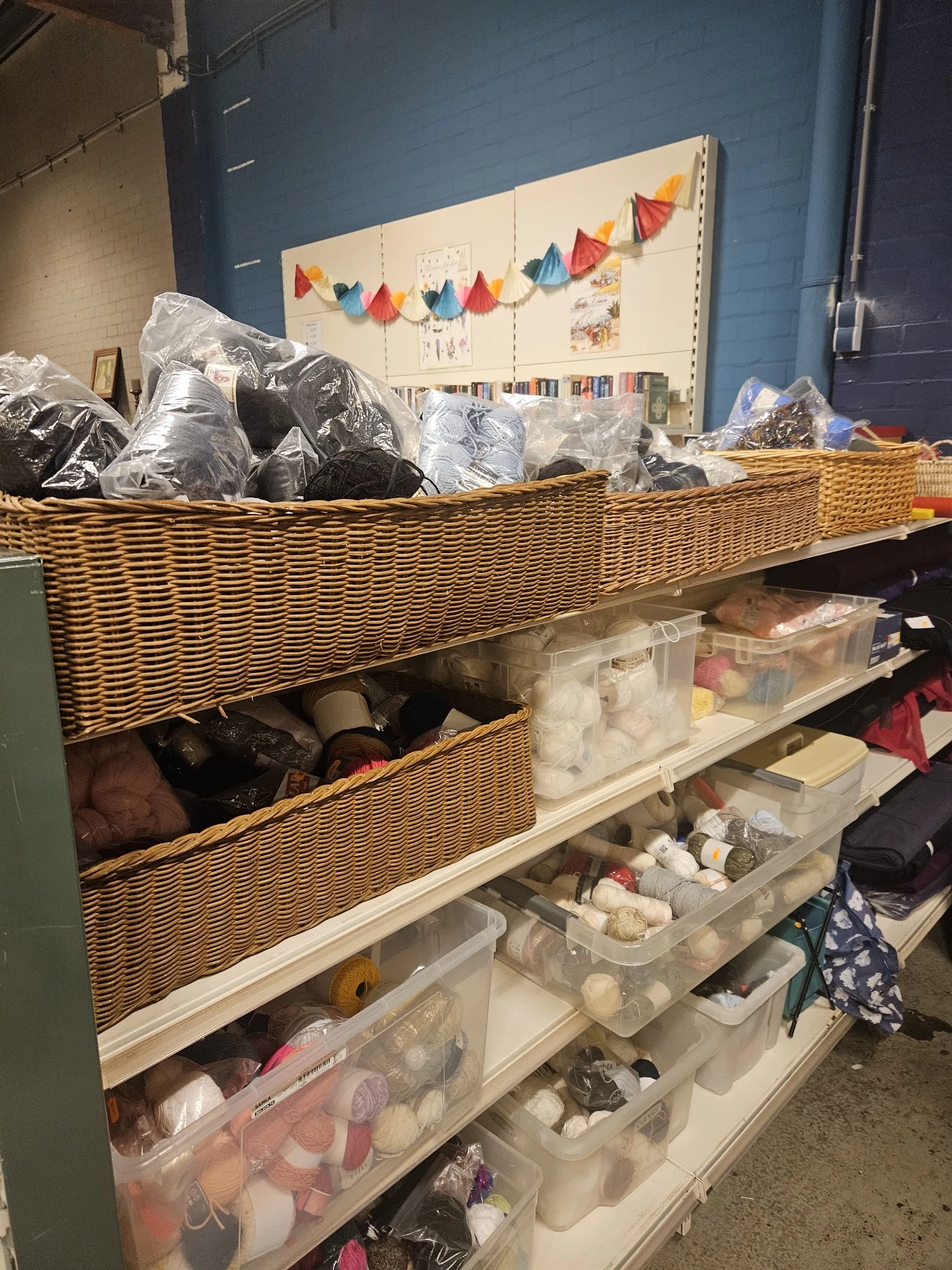 Wikkelmanden en plastic bakken met textiel en huishoudartikelen op stellingen