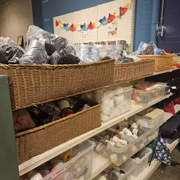 Wikkelmanden en plastic bakken met textiel en huishoudartikelen op stellingen