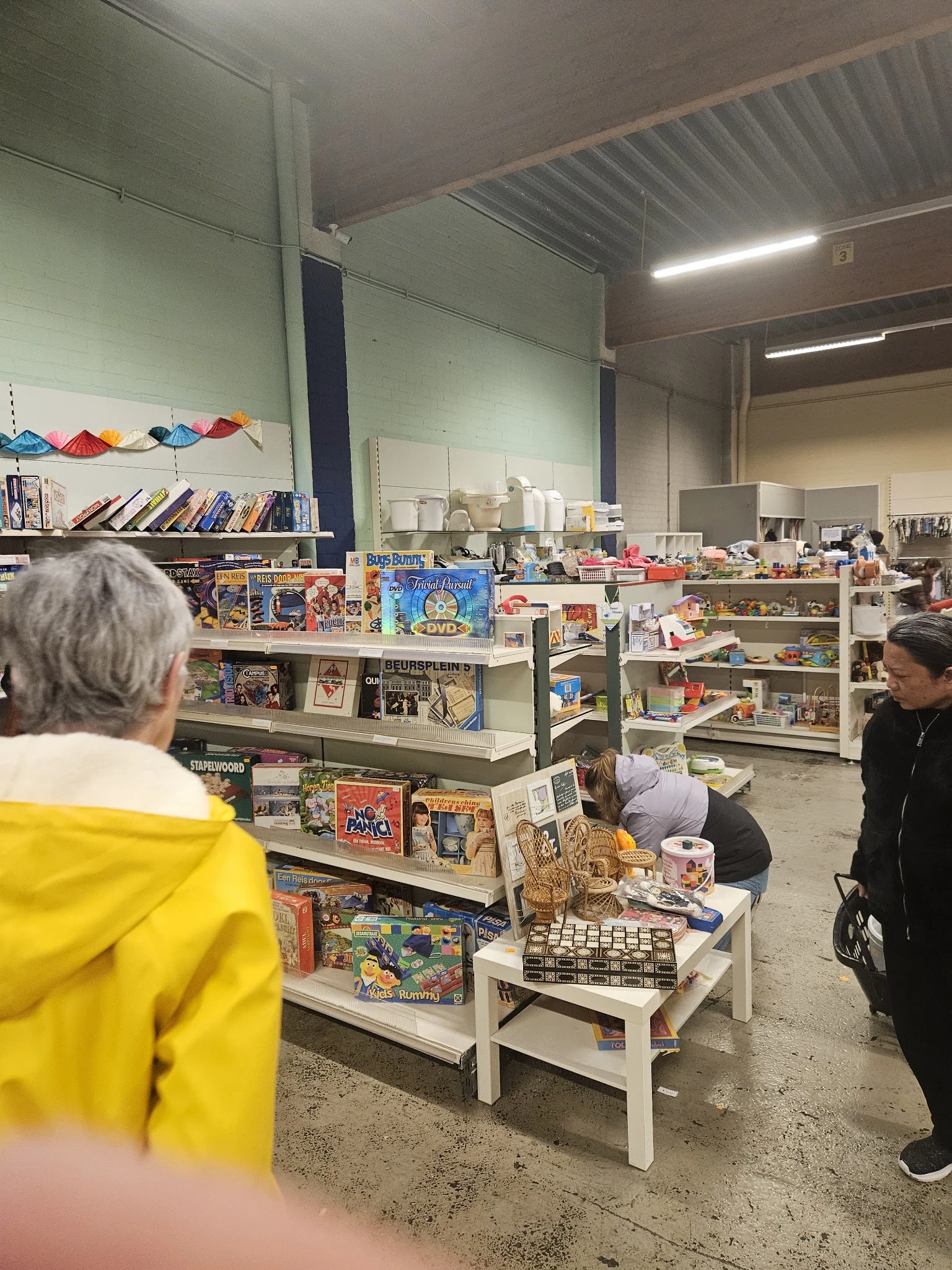 Winkelvloer met stellingen vol speelgoed, bordspellen, boeken en diverse tweedehandsartikelen; bezoekers kijken rond