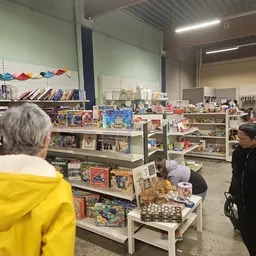 Winkelvloer met stellingen vol speelgoed, bordspellen, boeken en diverse tweedehandsartikelen; bezoekers kijken rond