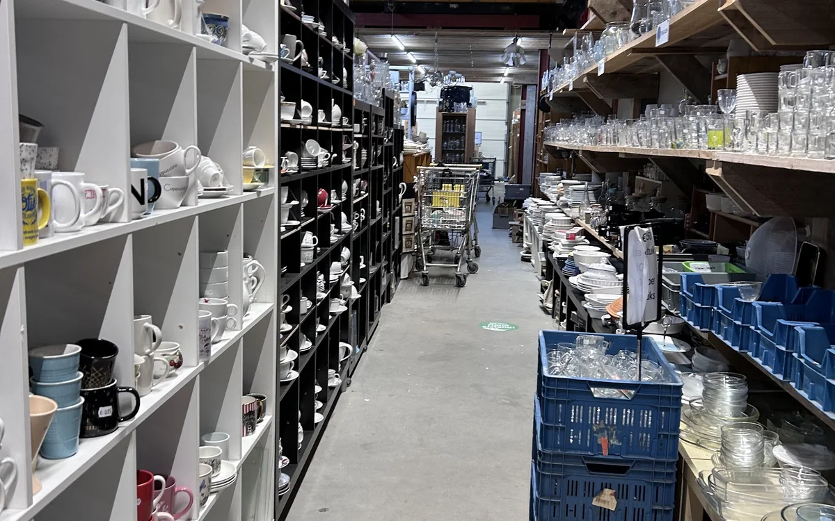 Winkelinterieur met stellingen vol serviesgoed, glazen en huishoudartikelen langs beide zijden van het middenpad