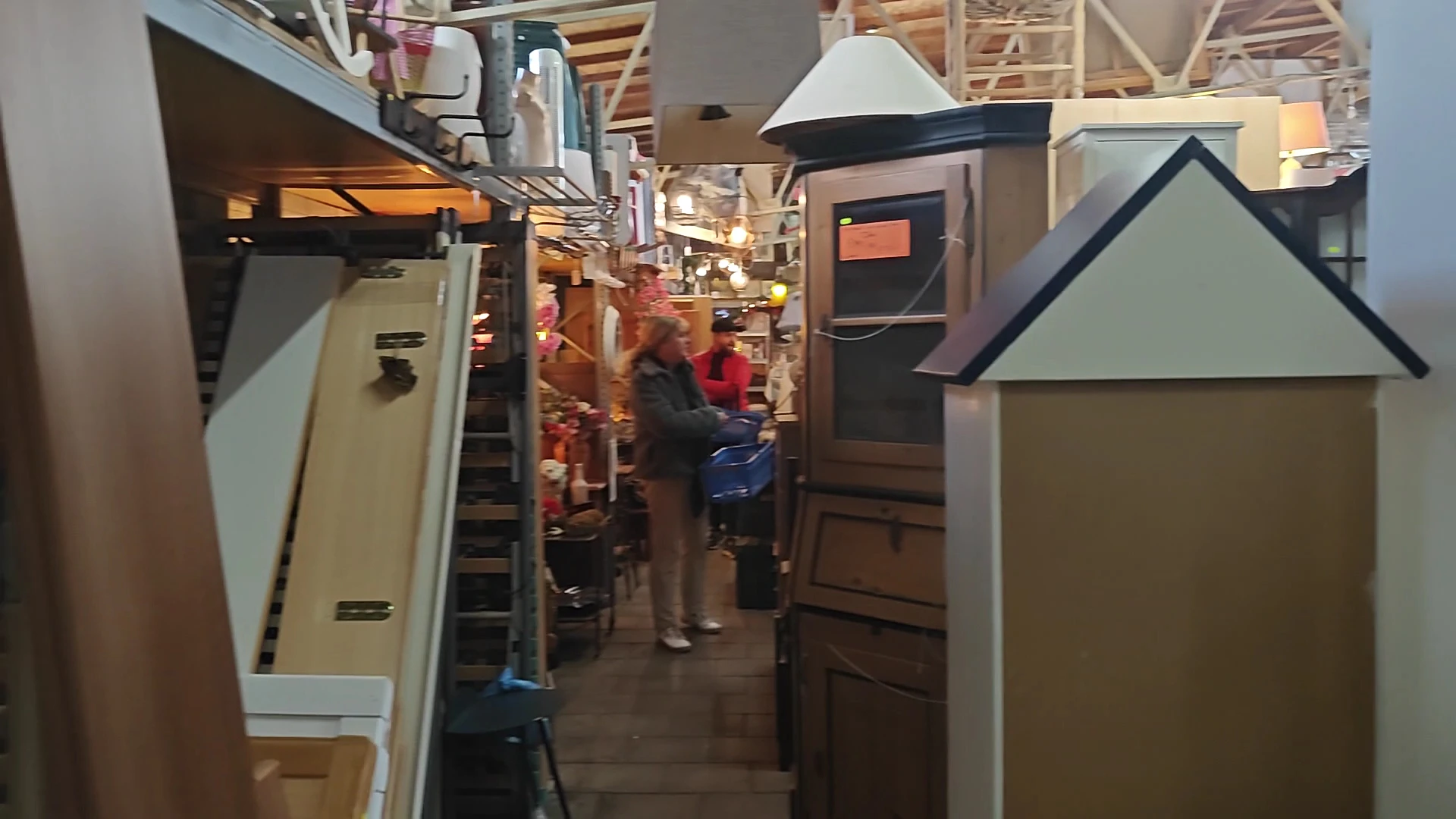 Binnenaanzicht van kringloopwinkel met stellingen, huisaccessoires en enkele bezoekers